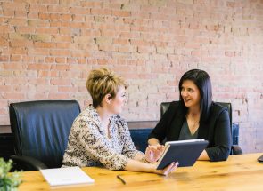 two white professional women at desk talking with notes