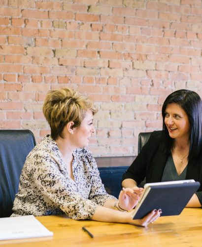 two white professional women at desk talking with notes two white professional women at desk talking with notes