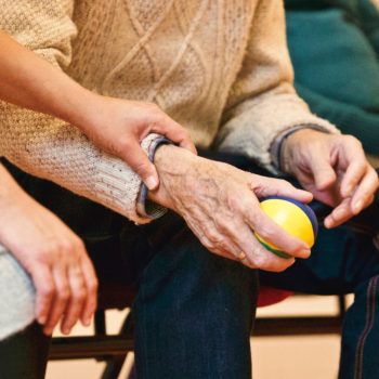An elderly person receives support from a caregiver, holding hands indoors, showcasing compassion.